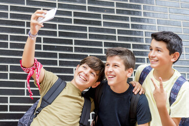 Glücklicher Schuljunge, der ein Selfie mit Freunden macht, die an einer Mauer stehen - CAVF61147