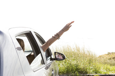 Frau winkt mit der Hand durch das Fenster, während sie im Auto gegen den klaren Himmel an einem sonnigen Tag fährt - CAVF61161