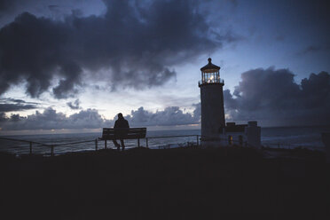 Silhouette man sitting on bench at beach against cloudy sky during sunset - CAVF61162