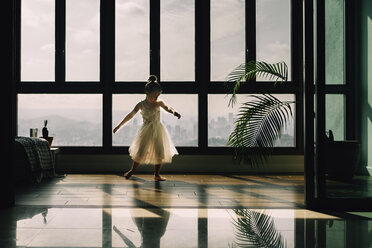 Full length of girl practicing ballet against window at home - CAVF61180