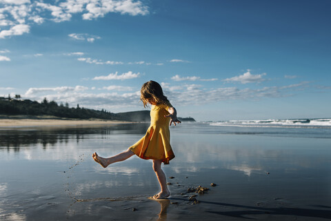 Seitenansicht von Mädchen spielen mit Sand am Strand gegen blauen Himmel während sonnigen Tag, lizenzfreies Stockfoto