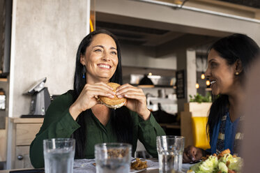 Happy female friends talking while eating food in cafeteria - CAVF61196