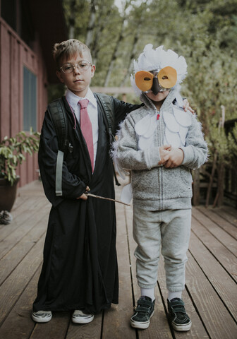 Porträt in voller Länge von Brüdern, die als Harry Potter und Eule verkleidet sind, auf dem Fußboden während Halloween, lizenzfreies Stockfoto