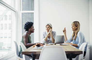Glückliche Geschäftsfrauen diskutieren am Konferenztisch in einem kreativen Büro - CAVF61208