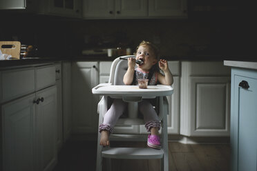 Süßes Baby Mädchen essen Essen, während auf Hochstuhl in der Küche zu Hause sitzen - CAVF61220