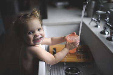 Porträt eines lächelnden, hemdsärmeligen kleinen Mädchens mit unordentlichem Mund, das Wasser in ein Glas zu Hause füllt - CAVF61221