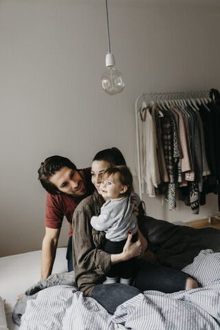 Glückliche Familie mit einem kleinen Mädchen, das zu Hause auf dem Bett sitzt, lizenzfreies Stockfoto
