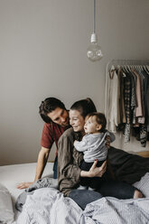 Happy family with baby girl sitting on bed at home - LHPF00467