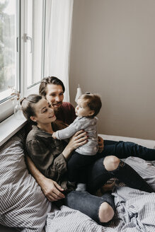 Happy family with baby girl sitting on bed at home - LHPF00468