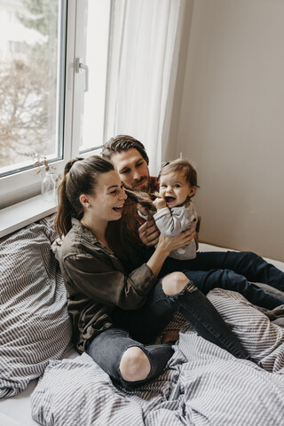 Glückliche Familie mit einem kleinen Mädchen, das zu Hause auf dem Bett sitzt, lizenzfreies Stockfoto