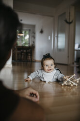 Baby girl lying on the floor playing with motor skill toy - LHPF00476