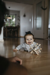 Happy baby girl lying on the floor playing with motor skill toy - LHPF00478