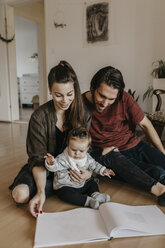 Happy family with baby girl sitting on the floor at home looking at photo album - LHPF00481