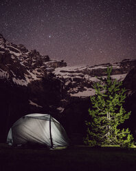 Illuminated tent on field by mountain against star field at night - CAVF61244