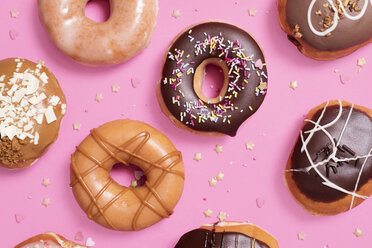 Overhead-Ansicht von verschiedenen Donuts mit Konfetti auf rosa Hintergrund angeordnet - CAVF61299