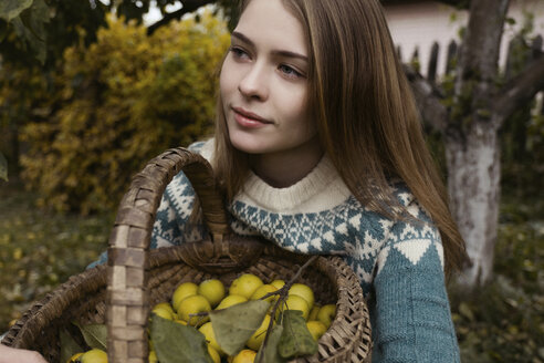 Close-up of thoughtful woman holding wicker basket with lemons while sitting at yard - CAVF61324