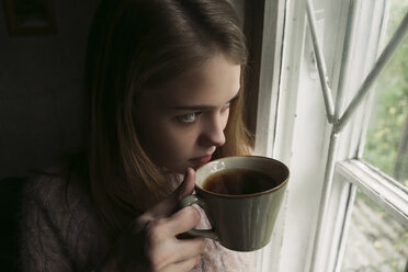 Close-up of thoughtful woman looking through window while having tea at home - CAVF61331