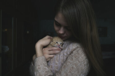Nahaufnahme einer Frau, die ein süßes Kätzchen hält, während sie zu Hause in der Dunkelkammer steht - CAVF61334