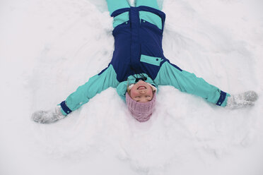 High angle view of woman with eyes closed making snow angel on field - CAVF61336