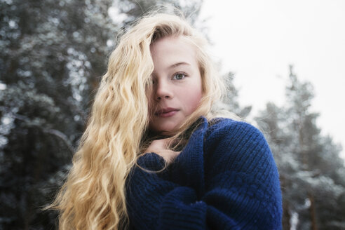 Low angle portrait of woman with blond hair standing against trees in forest during winter - CAVF61341