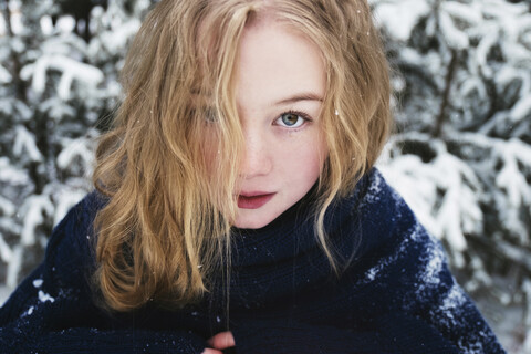 Nahaufnahme einer Frau mit blondem Haar, die im Winter vor Bäumen im Wald steht, lizenzfreies Stockfoto