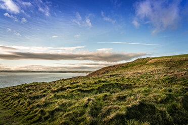 Scenic view of sea by green hill against blue sky during sunset - CAVF61358