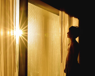 Seitenansicht eines nachdenklichen Jungen ohne Hemd am Fenster in der Dunkelkammer zu Hause - CAVF61409