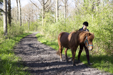 Woman with horse walking on footpath in forest - CAVF61423