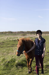 Frau mit Pferd spazieren auf grasbewachsenem Feld gegen den Himmel an einem sonnigen Tag - CAVF61426