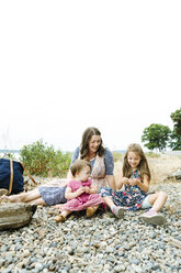 Glückliche Mutter schaut auf süße Töchter spielen mit sitzen auf Kieselsteinen gegen klaren Himmel - CAVF61442