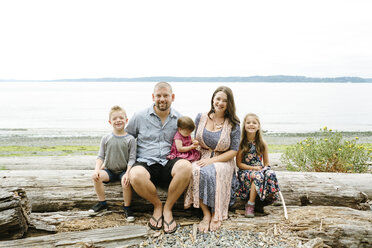 Portrait of happy family sitting on log at beach against clear sky - CAVF61446