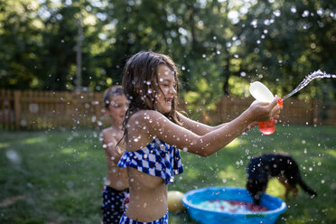 Playful siblings playing with water bombs at backyard - CAVF61456