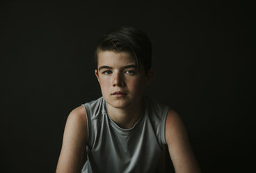 Porträt eines selbstbewussten Jungen, der vor einem schwarzen Hintergrund sitzt - CAVF61468