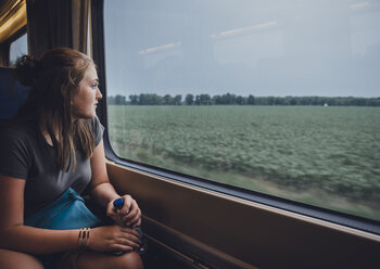 Teenage girl looking through window while traveling in train - CAVF61478