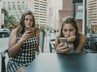 Female friends using smart phones while sitting at sidewalk cafe - CAVF61485