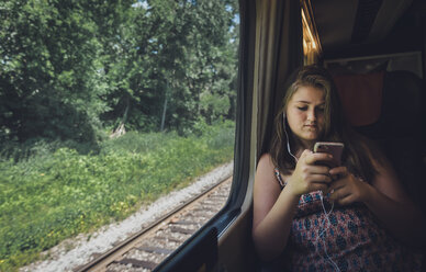 Teenage girl using smart phone while traveling in train - CAVF61486