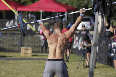 Rear view of disabled shirtless man lifting deadlift while standing at park - CAVF61490