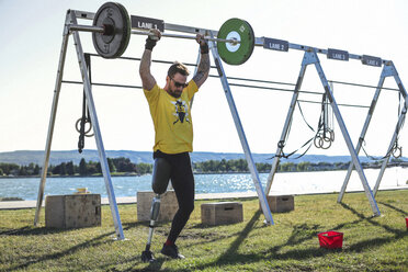 Männlicher Anpassungssportler beim Kreuzheben am See im Park an einem sonnigen Tag - CAVF61502