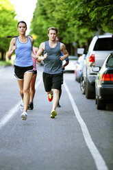 Portrait of athlete friends running on road against trees in city - CAVF61510