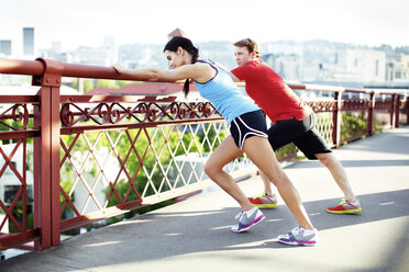 Athlete friends exercising on footbridge against sky in city - CAVF61516