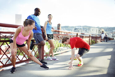 Freunde eines Sportlers unterhalten sich beim Sport auf einer Fußgängerbrücke gegen den klaren Himmel in der Stadt - CAVF61517