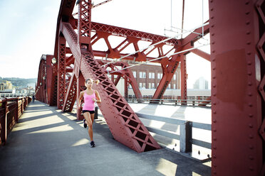 Female athlete running on footbridge in city - CAVF61521