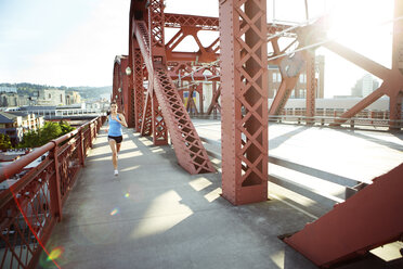 Weibliche Athletin läuft auf einer Fußgängerbrücke in der Stadt an einem sonnigen Tag - CAVF61522