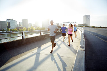 Athletenfreunde laufen auf einer Brücke gegen den Himmel in der Stadt an einem sonnigen Tag - CAVF61525