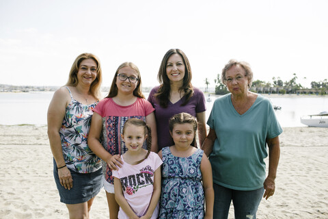 Porträt einer lächelnden weiblichen Mehrgenerationenfamilie, die am Strand vor dem Himmel steht, lizenzfreies Stockfoto