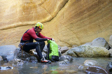 Side view of male hiker with backpack sitting on rocks in river - CAVF61578