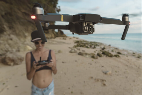 Indonesien, Bali, Nusa Dua, Frau fliegt Drohne am Strand - KNTF02711