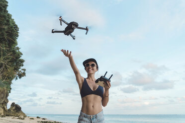 Indonesien, Bali, Nusa Dua, Frau fliegt Drohne am Strand - KNTF02714