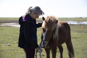 Seitenansicht einer Frau, die ein geknotetes Seil hält, während sie bei einem Pferd auf einem Feld an einem sonnigen Tag steht - CAVF61591