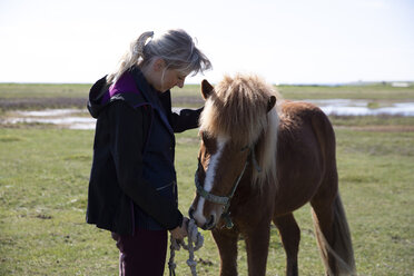 Side view of woman holding knotted rope while standing by horse on field during sunny day - CAVF61591